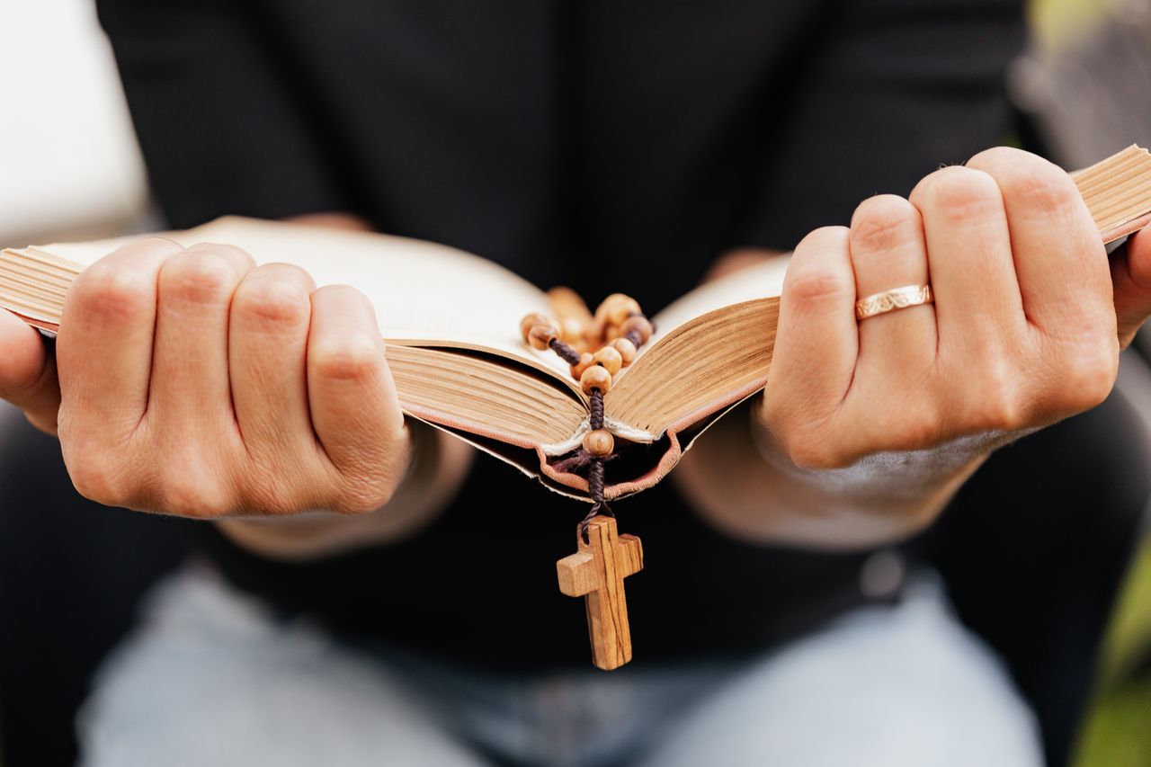 Home A close-up of hands holding an open Bible with a rosary, symbolizing faith.