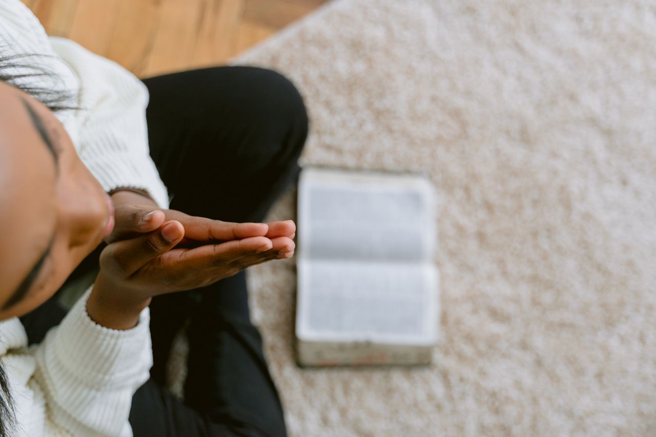 Home High angle view of a woman in prayer with an open Bible, symbolizing devotion and faith.